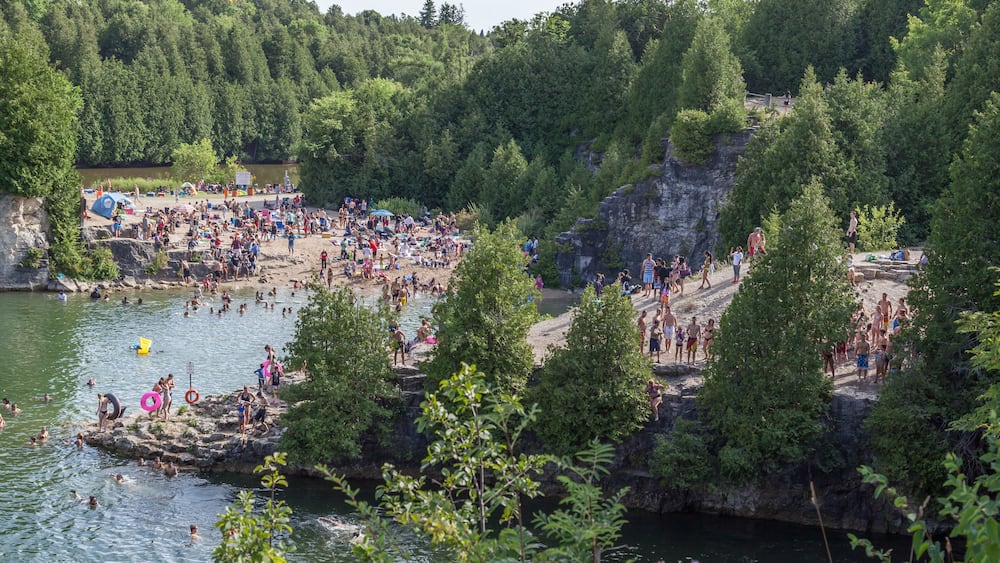 A crowded riverside beach with people swimming and sunbathing.