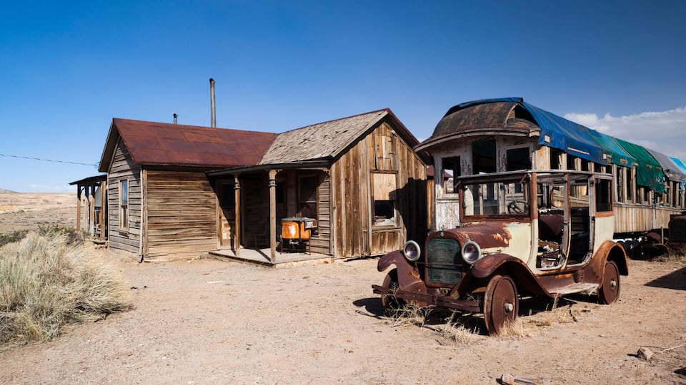 An old wooden building with a rusted car in front.