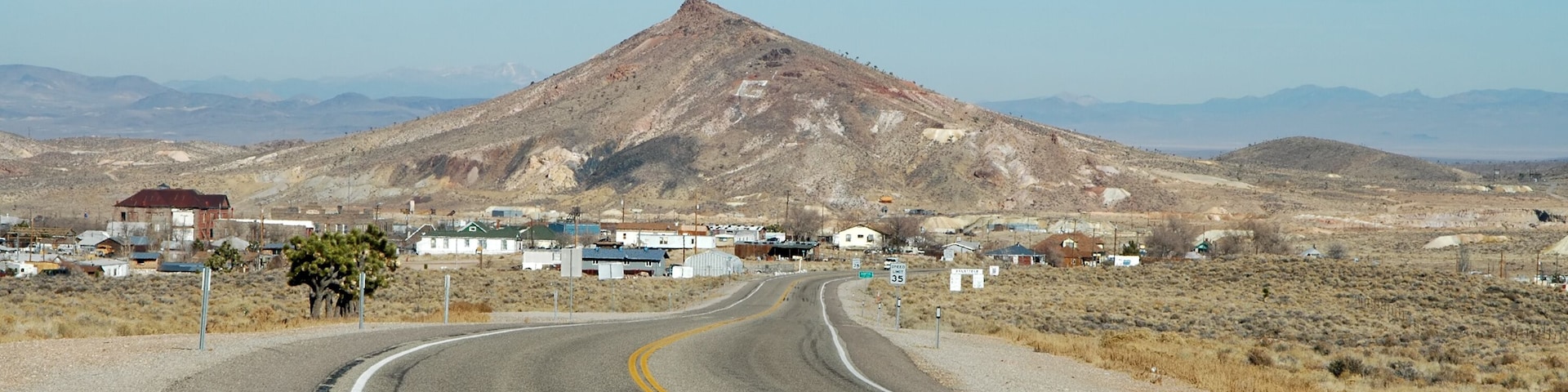 Uma estrada sinuosa que leva a uma pequena cidade, com casas e uma montanha ao fundo.