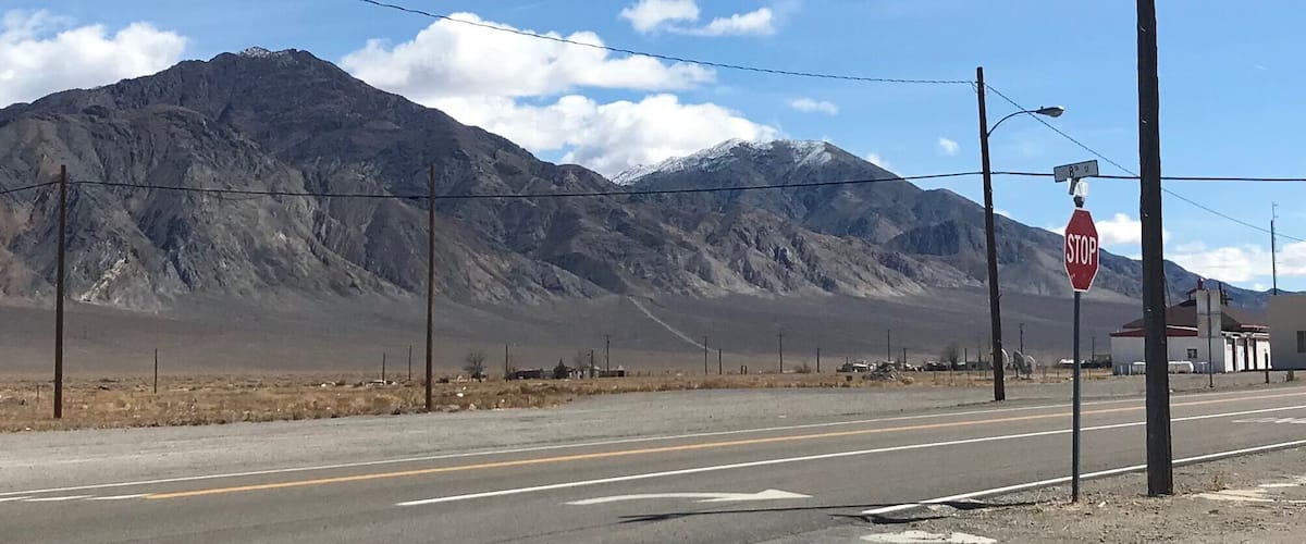 A road with a stop sign, power lines, and a mountain range in the background.