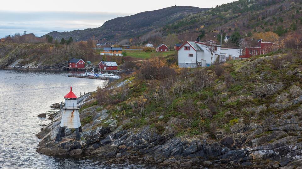 A coastal village with a lighthouse, red houses, and a boat docked near the shore.