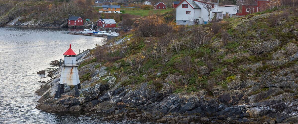 A coastal village with a lighthouse, red houses, and a boat docked near the shore.