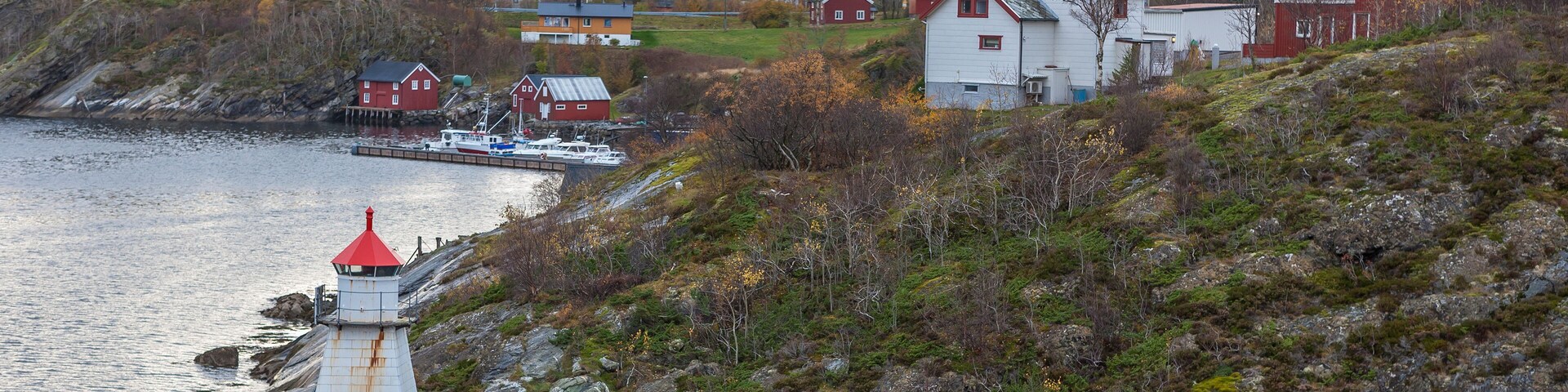 A coastal village with a lighthouse, red houses, and a boat docked near the shore.