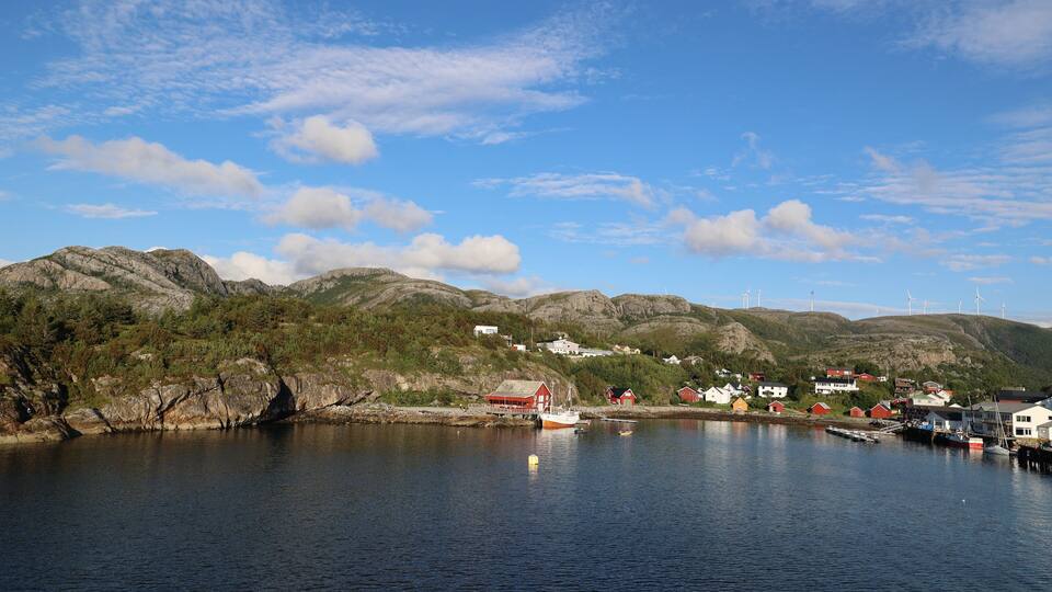 A coastal village with houses, boats, and wind turbines on the hills.