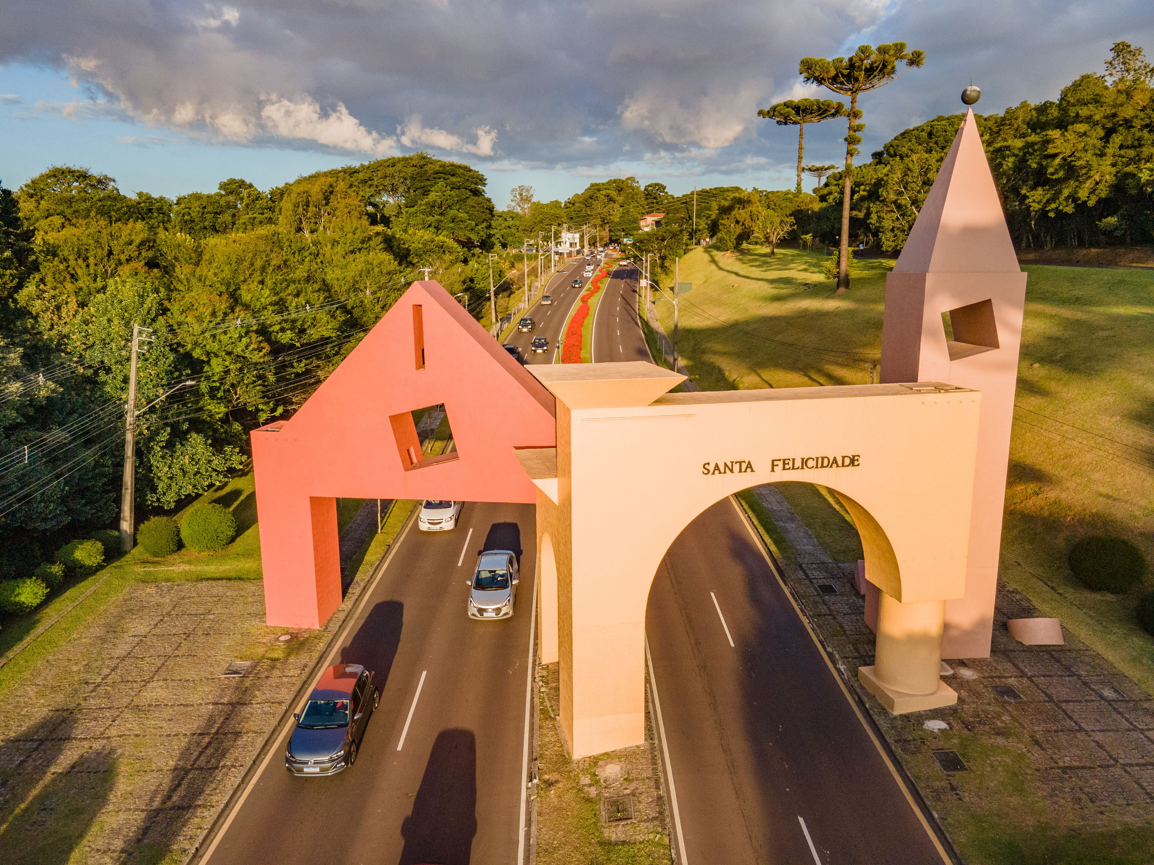 A road passing through a rural area with a large archway labeled "SANTA FELICIDADE" and a distinctive red house-like structure.
