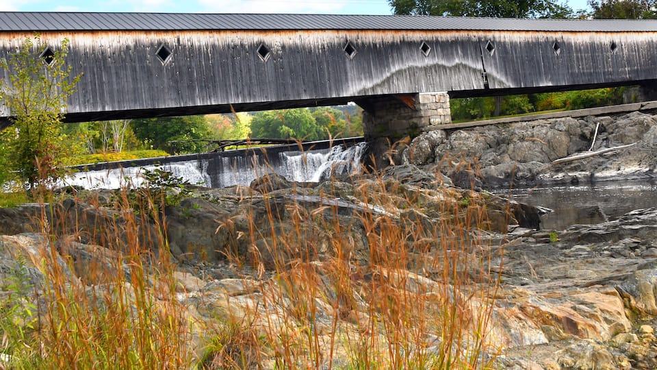 A wooden covered bridge over a rocky river.