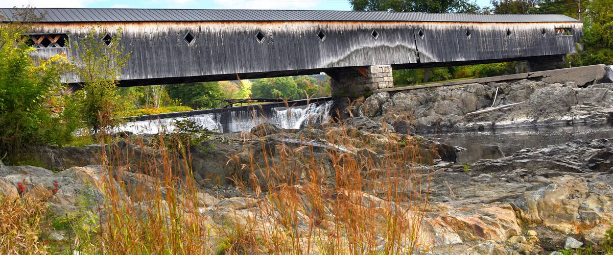 A wooden covered bridge over a rocky river.