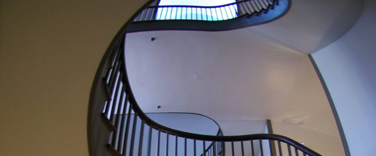 A spiral staircase with wooden railings and a mirrored wall reflecting the interior.