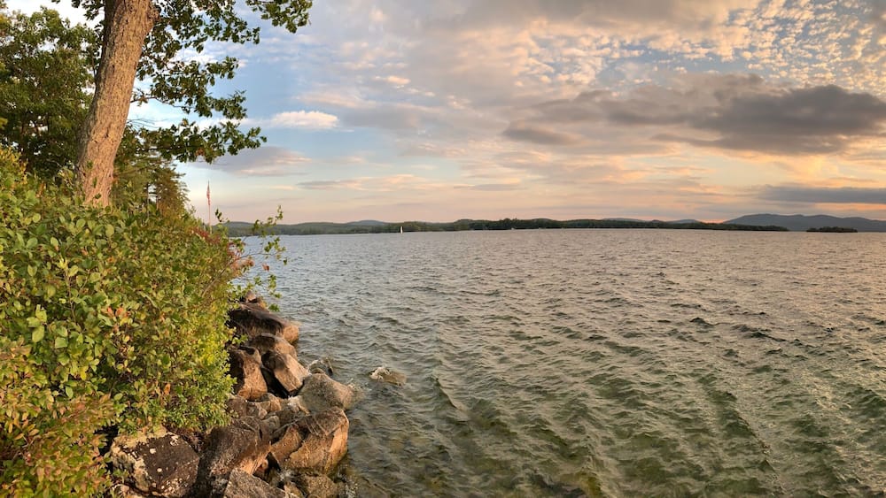 Un lac où le soleil se couche, entouré d’arbres et de rochers.