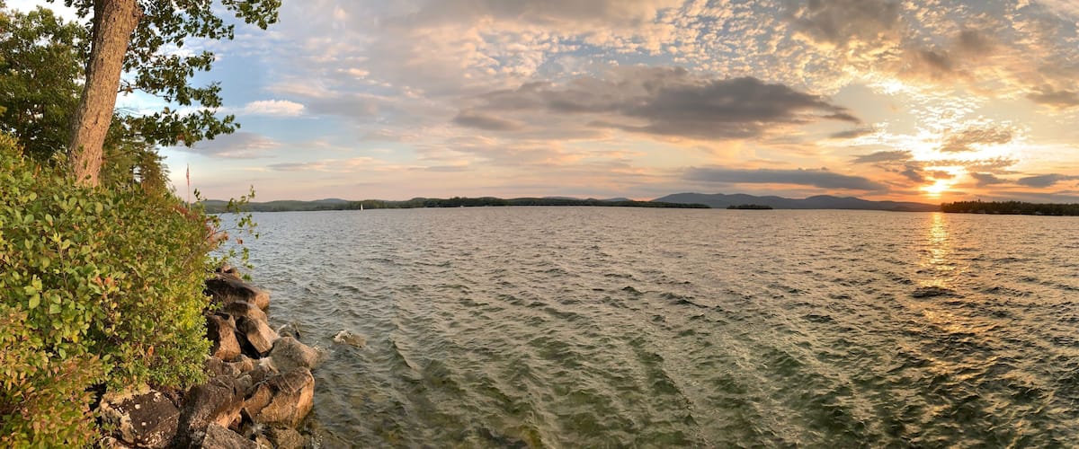 A lake with a sunset, surrounded by trees and rocks.