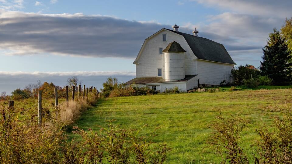 A white barn with a silo on a grassy hill.
