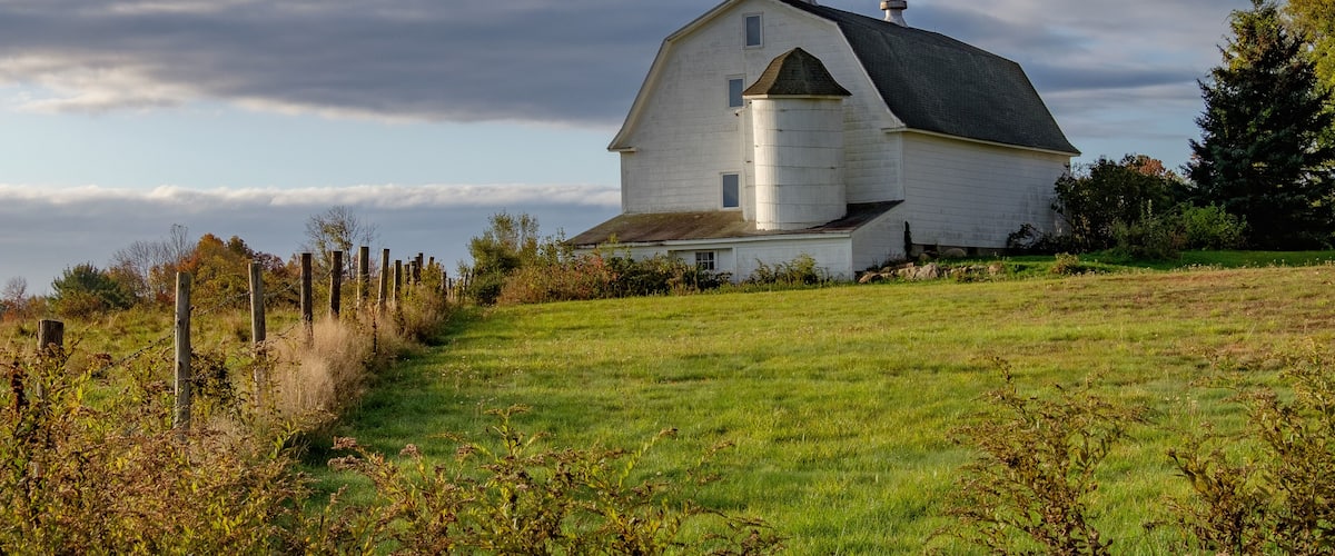 A white barn with a silo on a grassy hill.