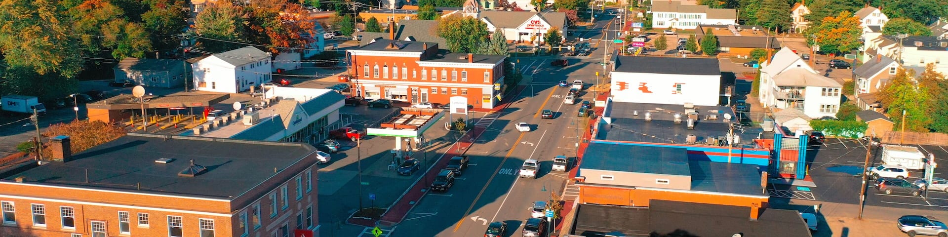 A town with a central street, buildings, and a forested hill in the background.