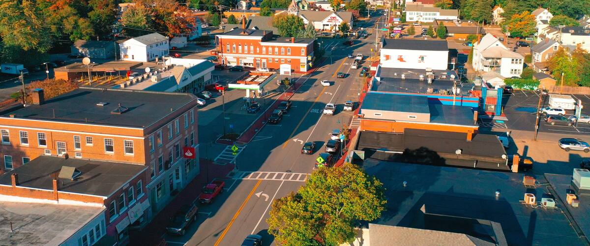 A town with a central street, buildings, and a forested hill in the background.