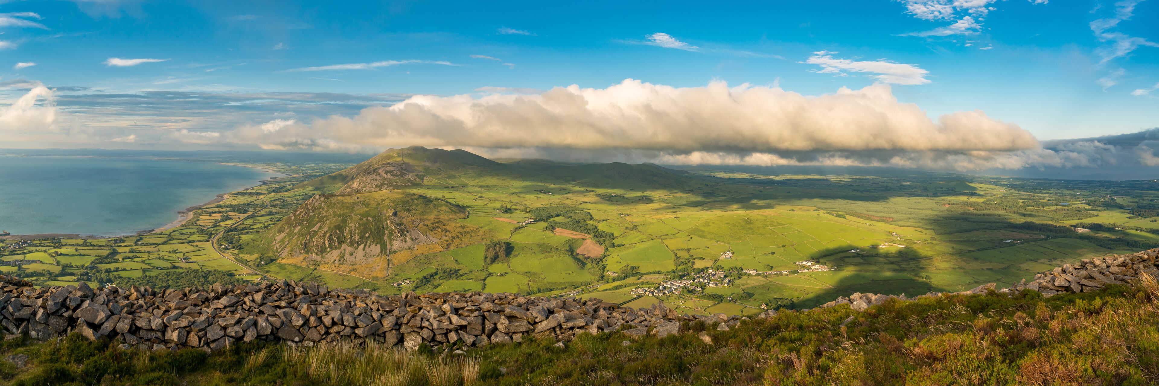 A coastal landscape with rolling hills, a stone wall, and a village.