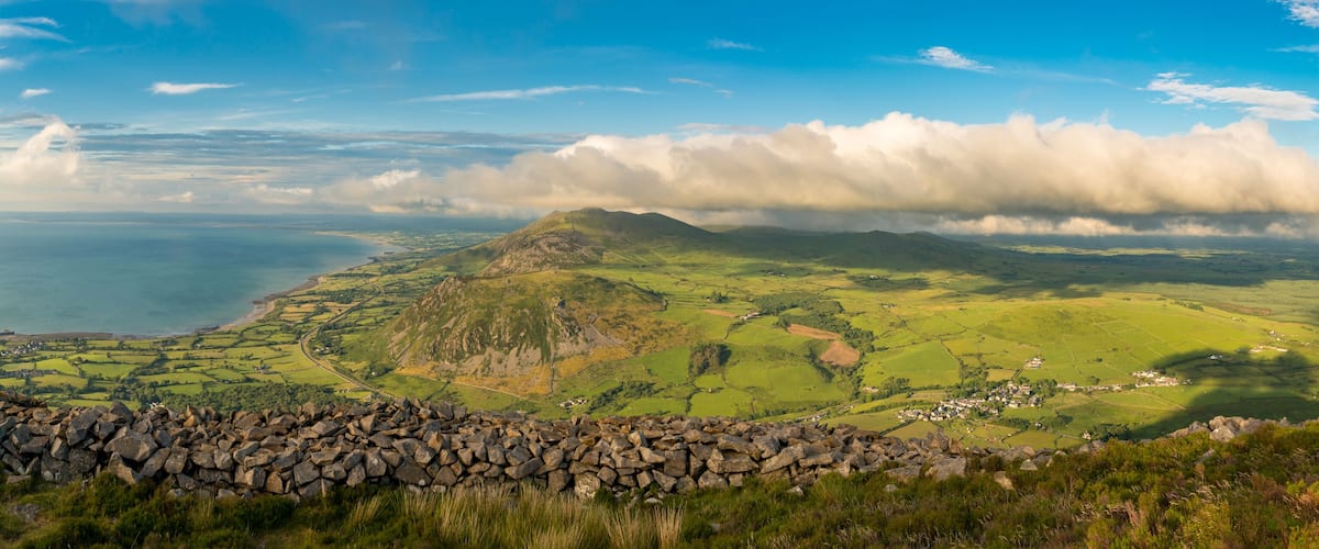 A coastal landscape with rolling hills, a stone wall, and a village.