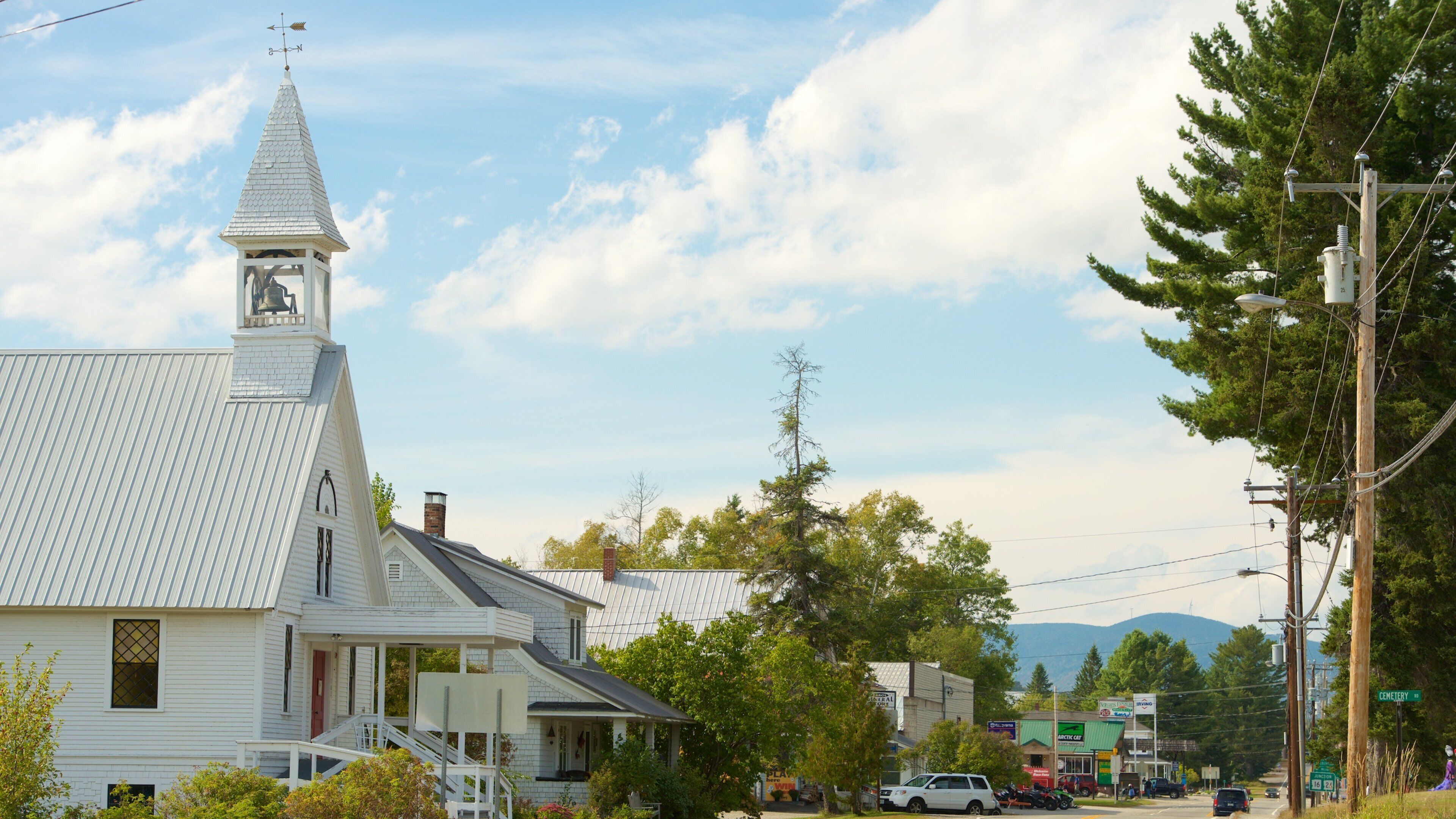 A white church with a steeple and a clock tower, surrounded by trees and a road with cars.