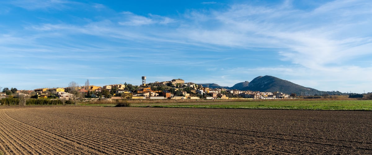 A rural landscape with a village, a mountain, and a plowed field.