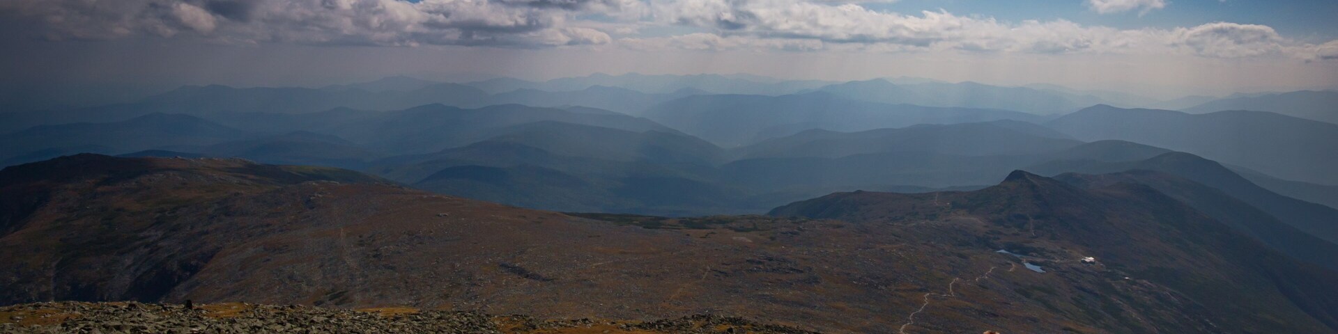 Dos personas descansando sobre una cresta rocosa de montaña, con vistas a cordilleras lejanas y un cielo despejado.