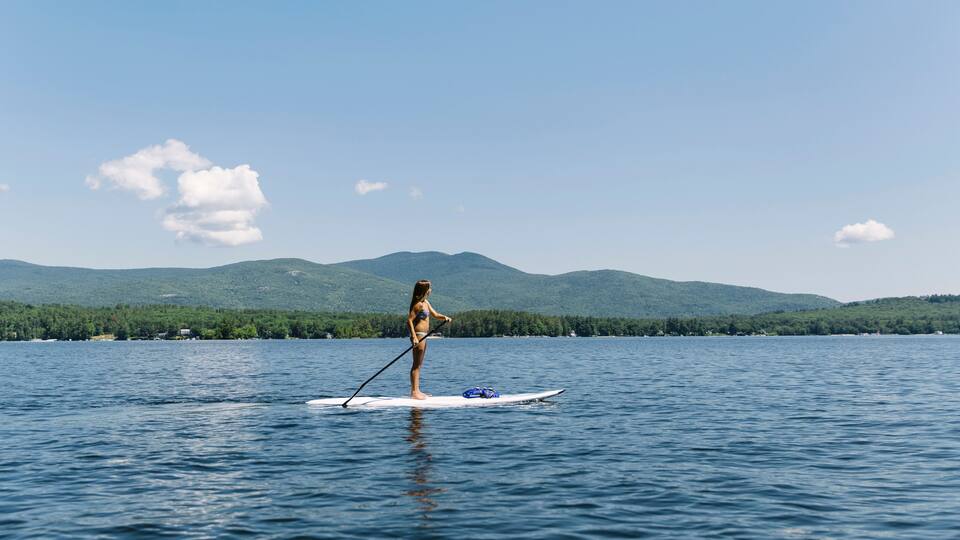 A person paddleboarding on a calm lake with mountains in the background.