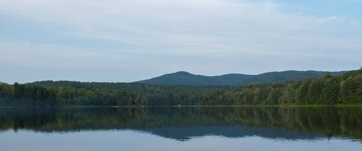 A calm lake with reflections of trees and mountains in the background.
