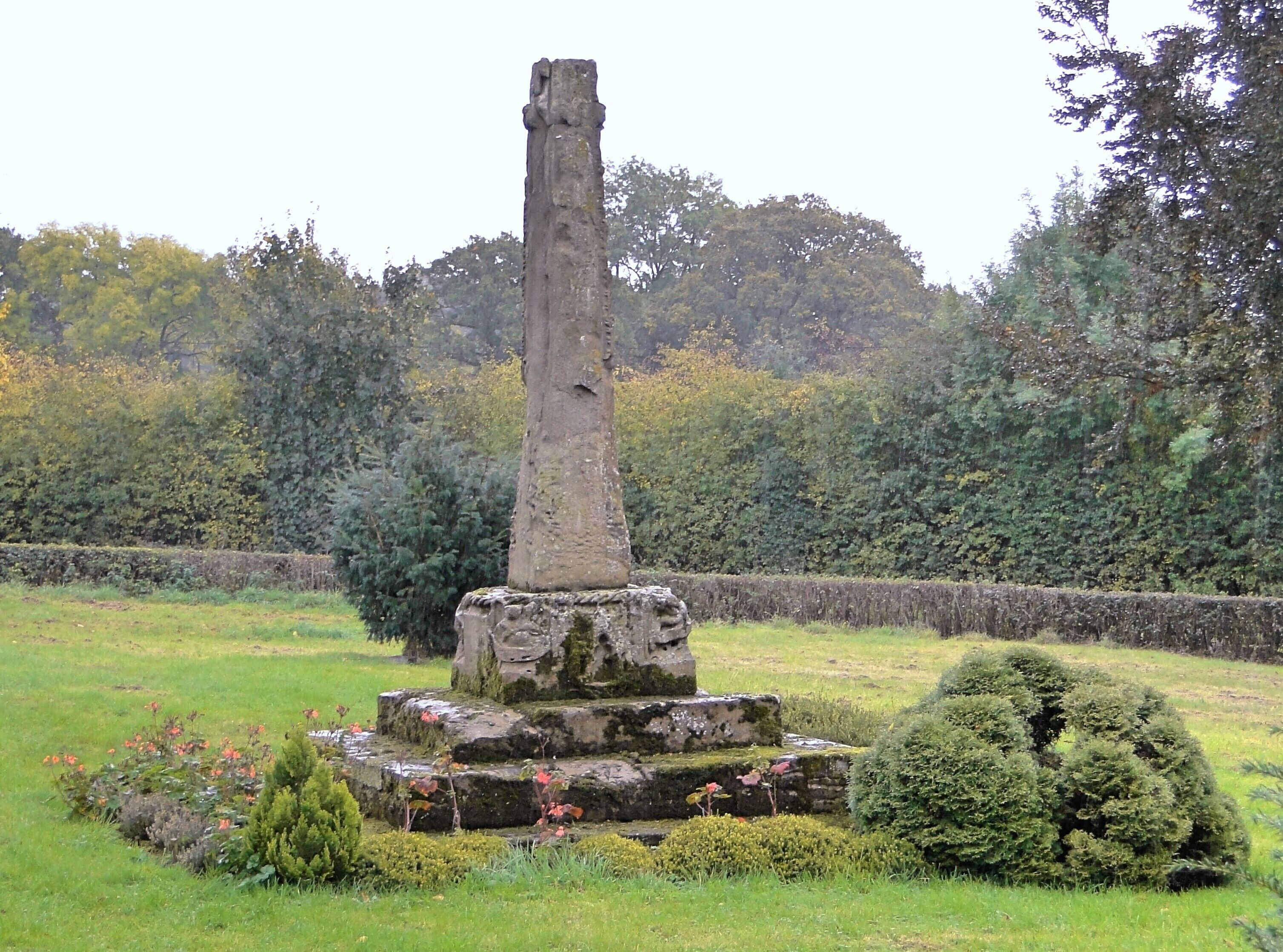 A standing stone monument surrounded by a well-maintained garden with flowers and shrubs.
