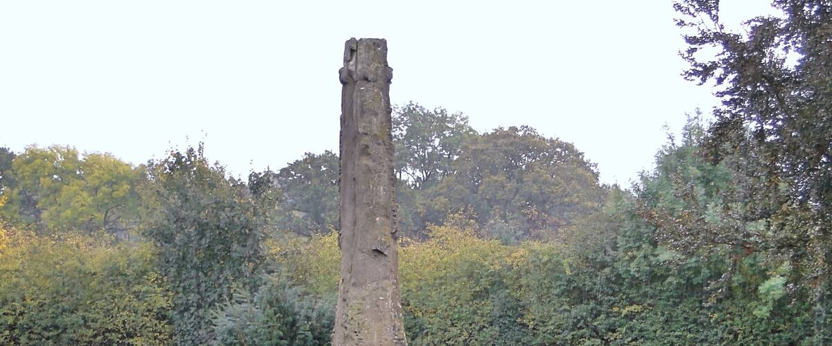 A standing stone monument surrounded by a well-maintained garden with flowers and shrubs.