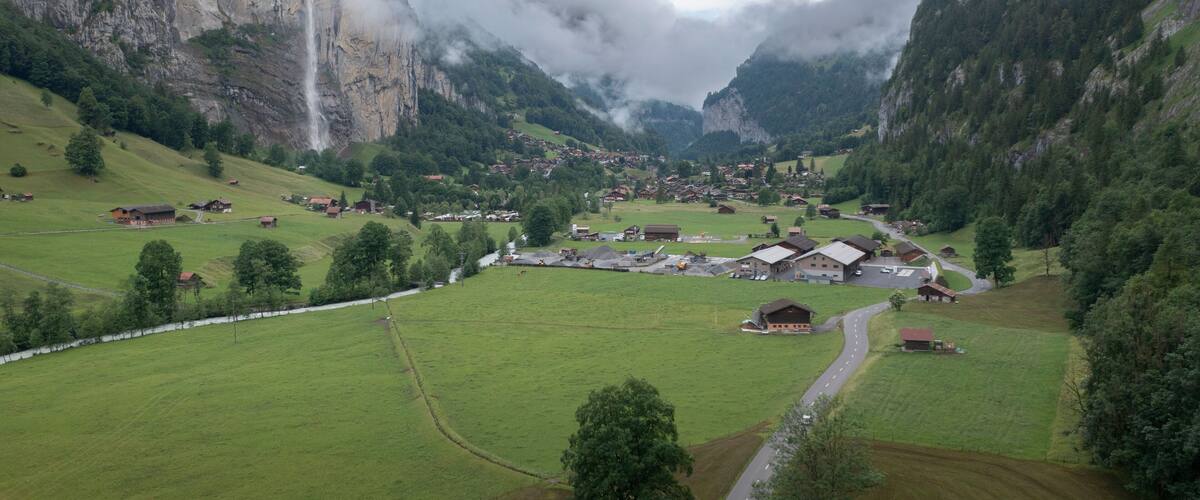 A valley with a waterfall, houses, and green fields.