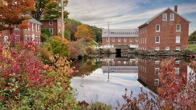 Colorful autumn scene at historic 19th-century textile mill town in Monadnock region of New Hampshire. Picturesque village of Harrisville with reflection of sky and red brick buildings on water.
