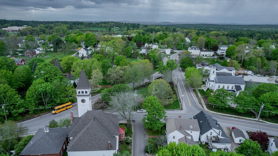 A rural town with a prominent church tower, a school bus, and lush greenery.