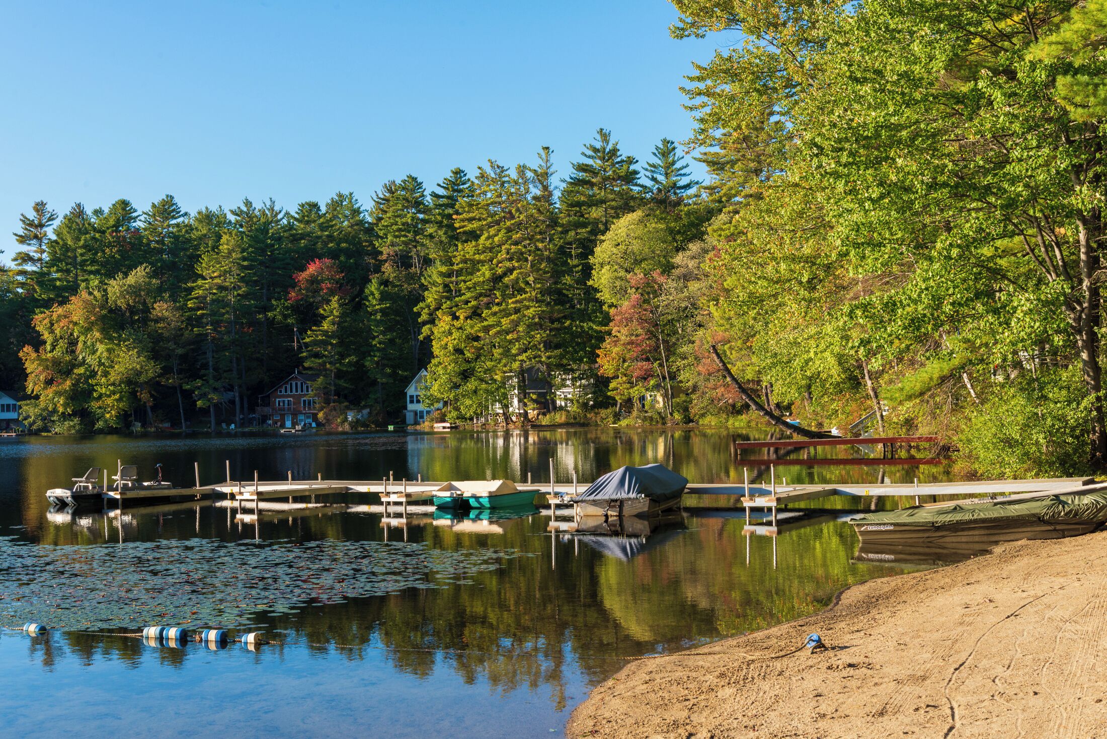 A lake with docked boats, a sandy beach, and surrounding trees.