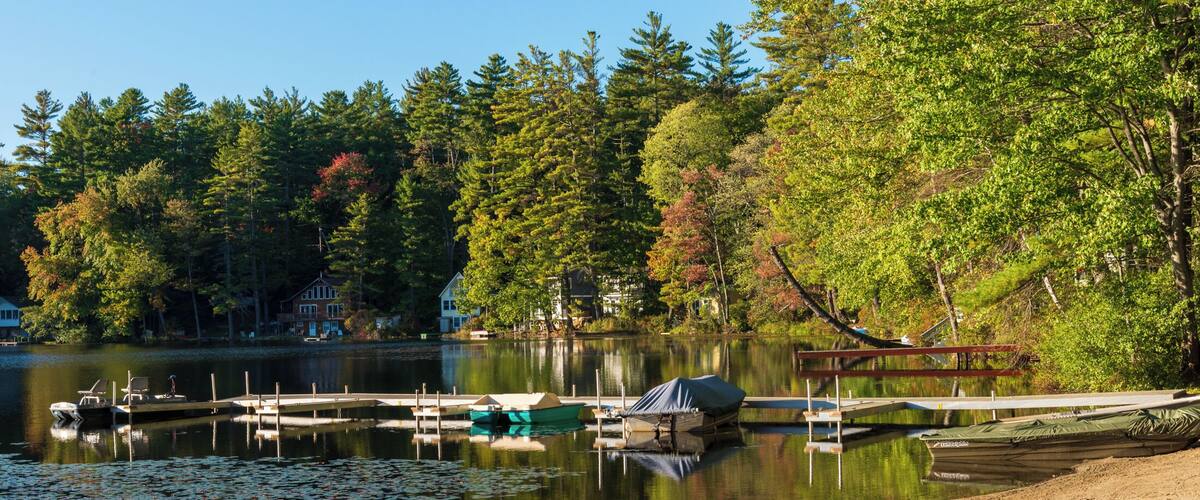 A lake with docked boats, a sandy beach, and surrounding trees.