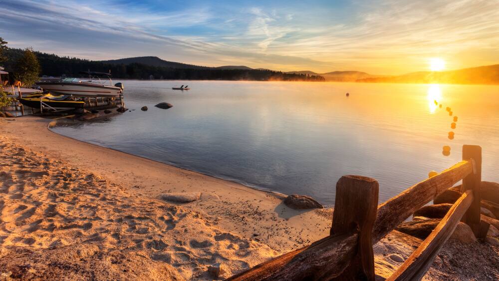 Mist rises from Merrymeeting Lake, as seen from the beach by the marina boat launch, New Durham, New Hampshire right after sunrise on a summer morning