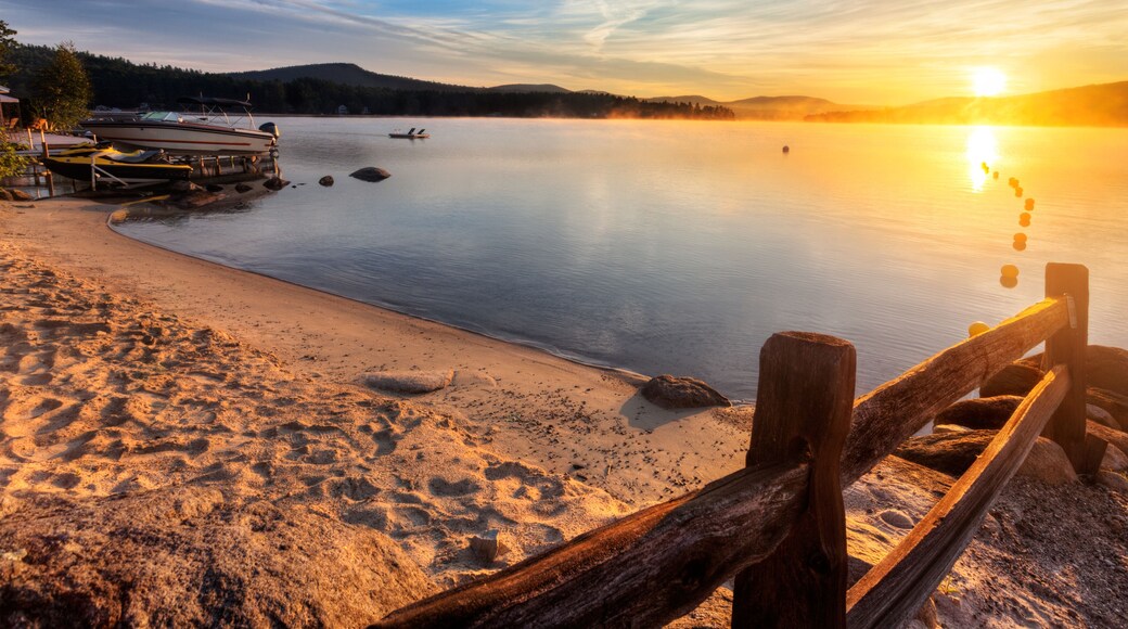 Mist rises from Merrymeeting Lake, as seen from the beach by the marina boat launch, New Durham, New Hampshire right after sunrise on a summer morning