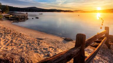 Mist rises from Merrymeeting Lake, as seen from the beach by the marina boat launch, New Durham, New Hampshire right after sunrise on a summer morning