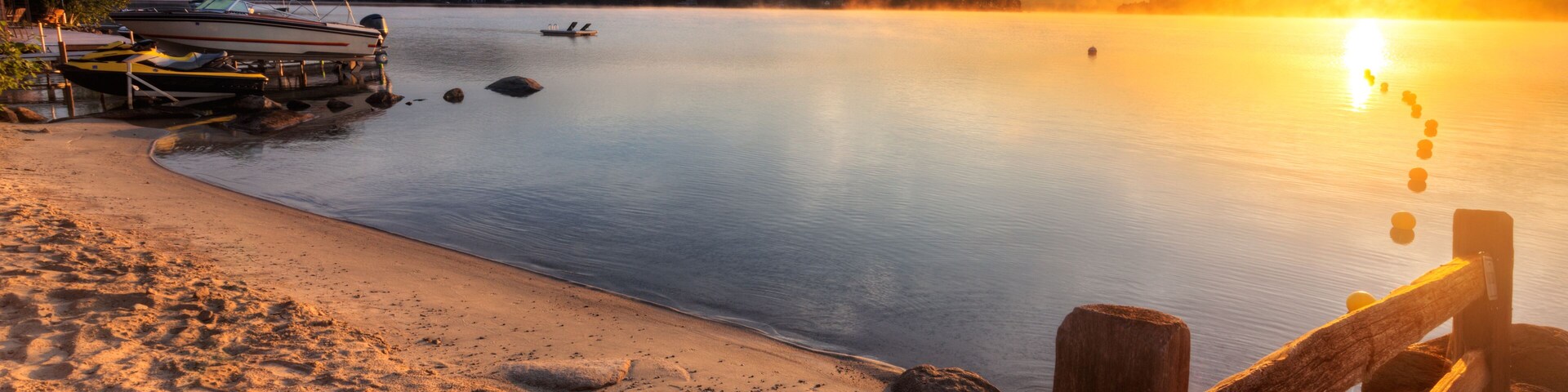 Mist rises from Merrymeeting Lake, as seen from the beach by the marina boat launch, New Durham, New Hampshire right after sunrise on a summer morning