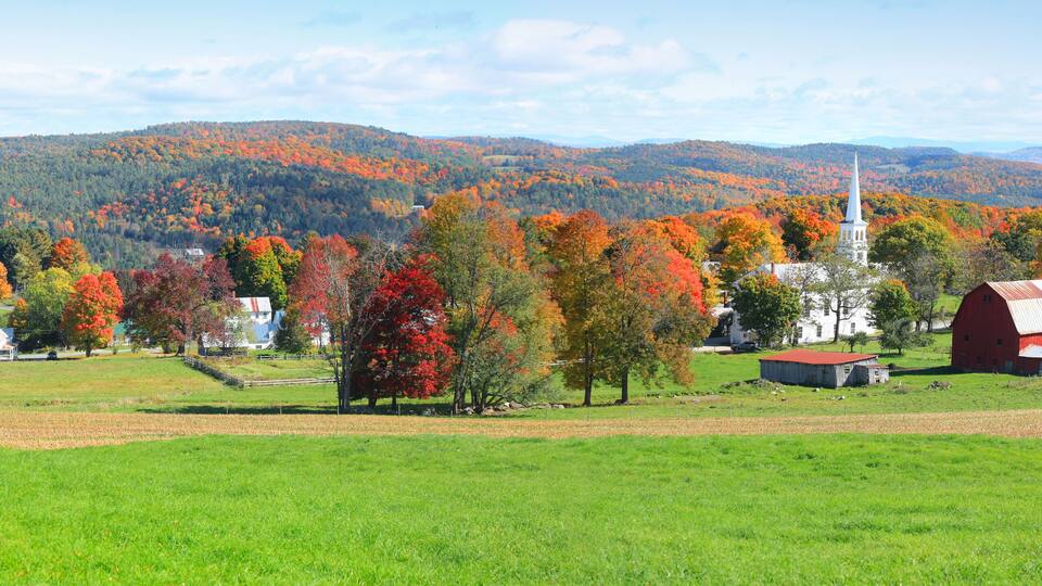 A rural landscape with a church, barns, and autumn-colored trees.