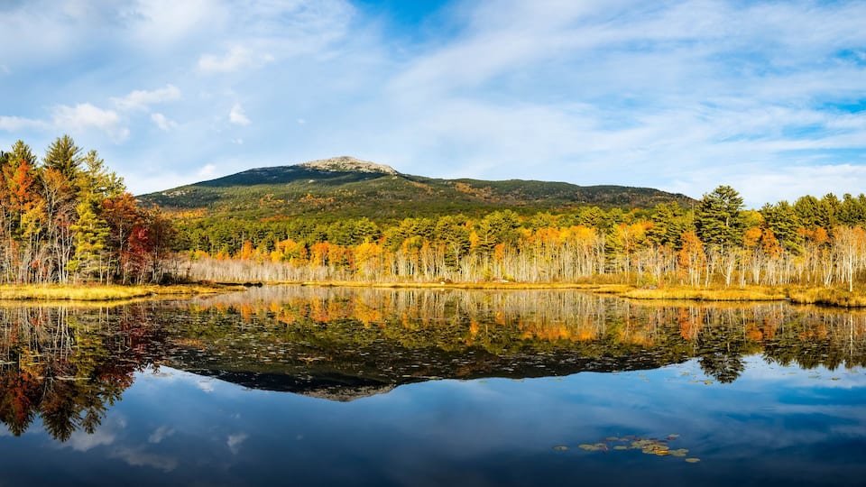 A calm lake reflecting autumn trees and a mountain in the background.