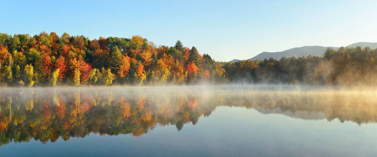 A calm lake reflecting colorful autumn trees and misty mountains in the distance.
