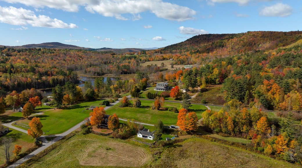 Aerial view of vibrant fall foliage painting the landscape around scattered houses and a tranquil pond, with rolling hills beyond, in the White Mountains. Sugar Hill, New Hampshire, United States.