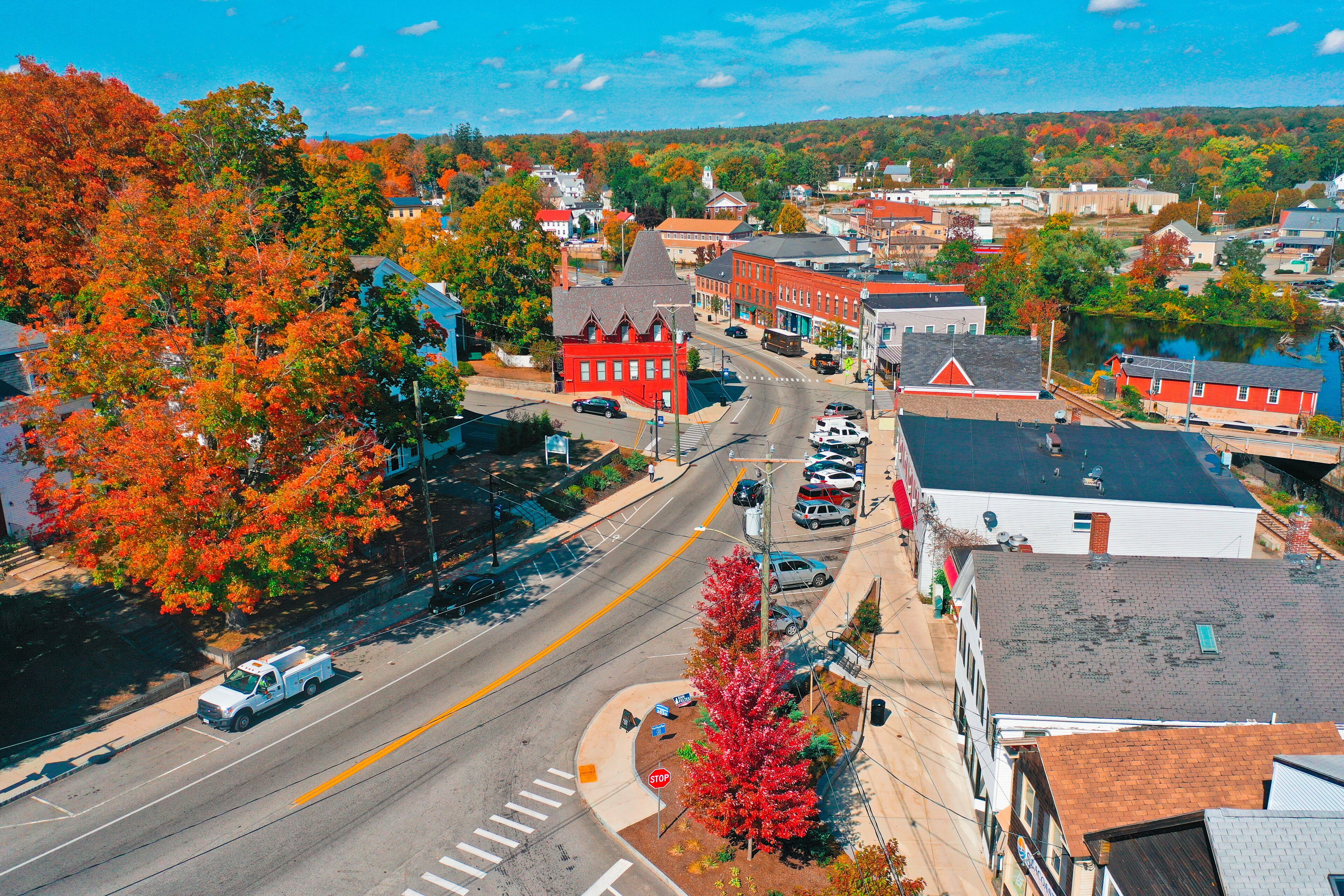 A town with autumn-colored trees, a river, and a mix of red and white buildings.