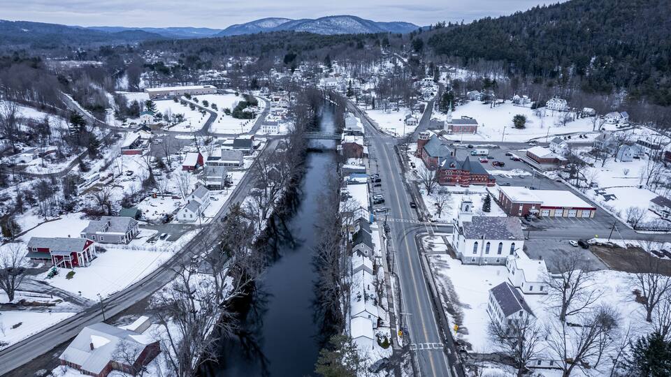 A snow-covered town with a river running through it, surrounded by mountains and trees.
