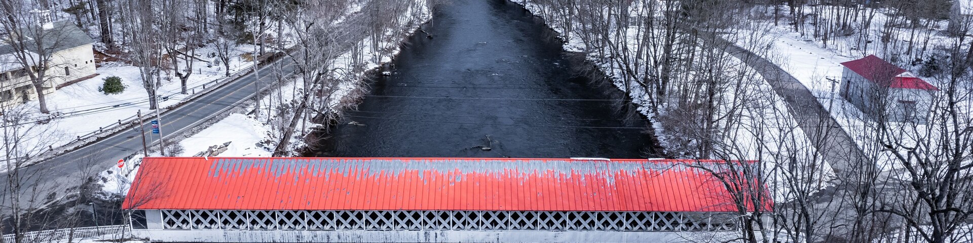 Un puente cubierto de nieve sobre un río con techo rojo, rodeado de árboles y edificios.