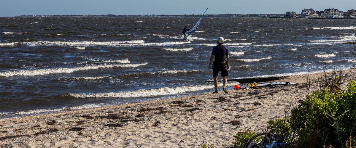 A beach with waves, a person with a kite, and houses in the distance.