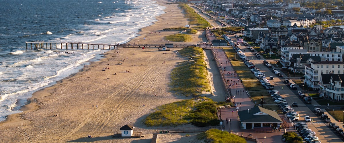 A coastal cityscape with a beach, a pier, and residential buildings.