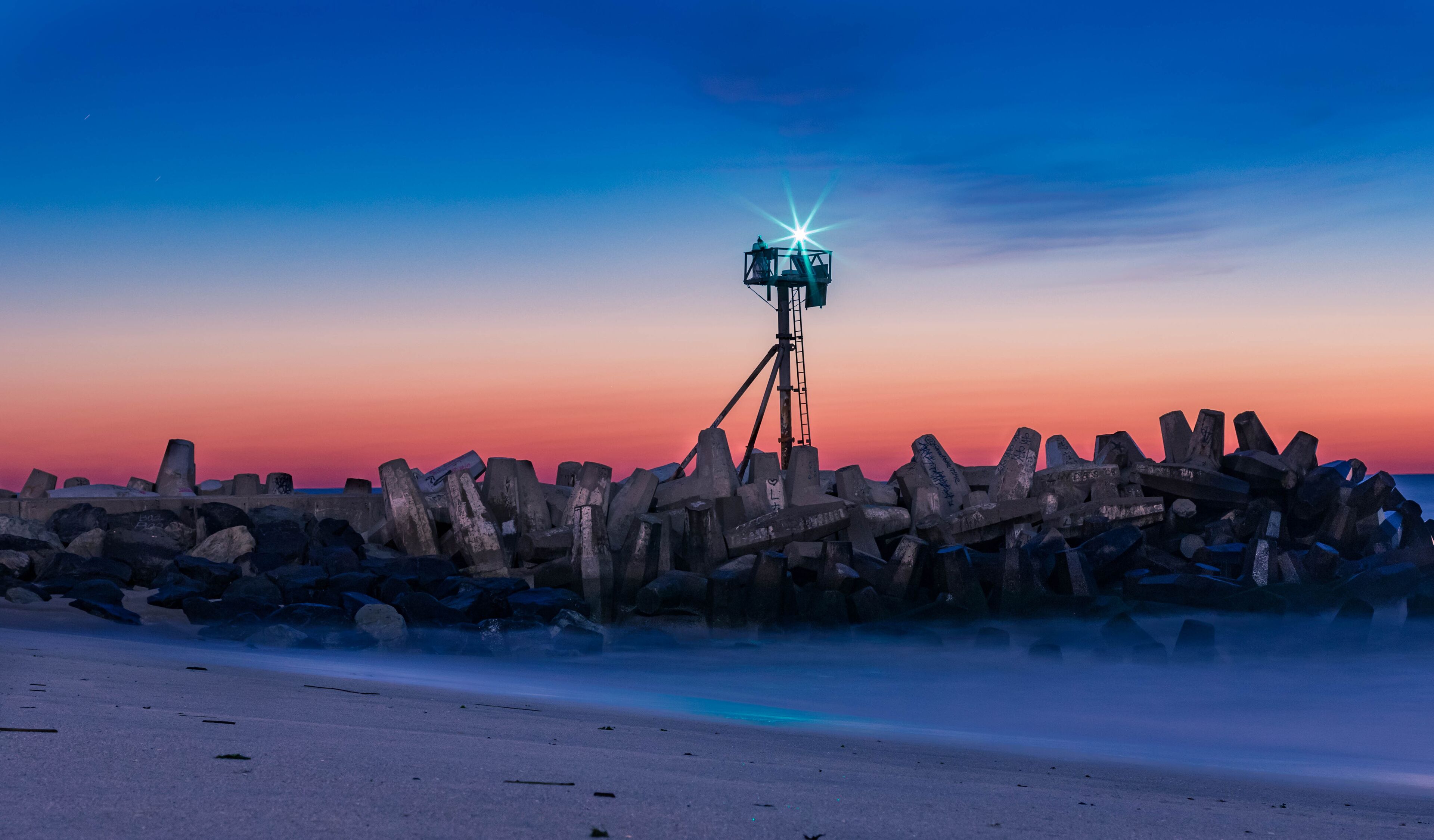 A sunset over a rocky shoreline with a tripod-mounted camera.