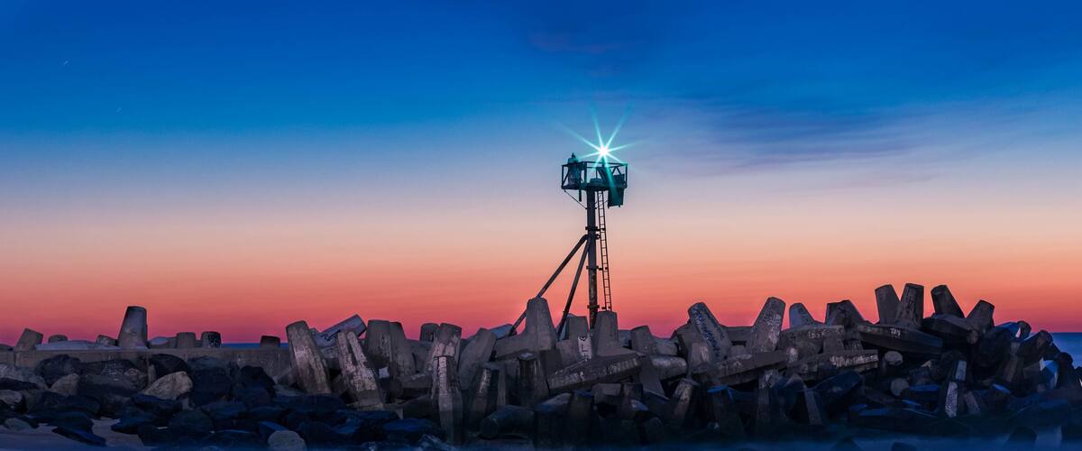 A sunset over a rocky shoreline with a tripod-mounted camera.