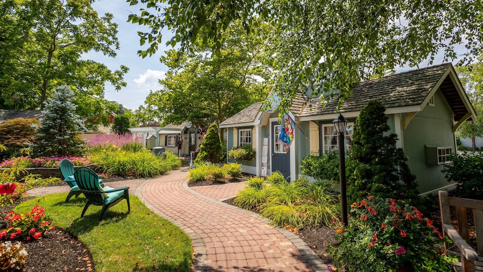 A garden with a brick pathway, benches, and a small building with a green roof.