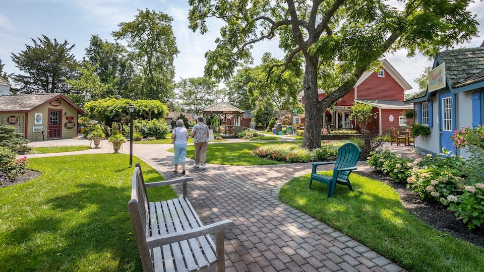 A garden with a wooden bench, a gazebo, and a red building with blue shutters.