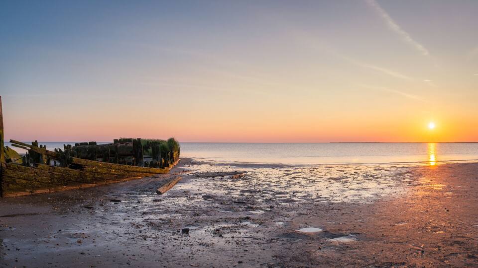A sunset over a beach with a wooden structure and driftwood.